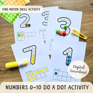 May include: Educational fine motor skill activity featuring number cards 1, 2, 3, and 7, with dot outlines for each number. The cards include a ten frame and the text "Let's count!" and "Numbers 0-10 Do a Dot Activity". Includes colorful pom-poms, a yellow marker, and tweezers.