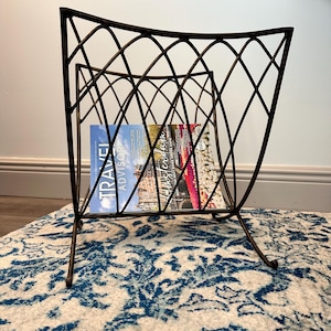 Puede incluir: Un revistero de metal negro con un diseño curvo y una revista titulada "Travel Advisor" en su interior.