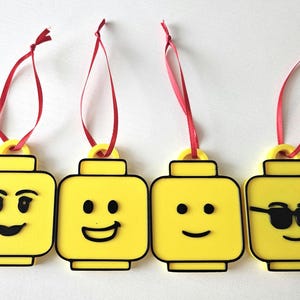 May include: Four yellow Lego minifigure ornaments with different facial expressions. Each ornament has a red ribbon for hanging.