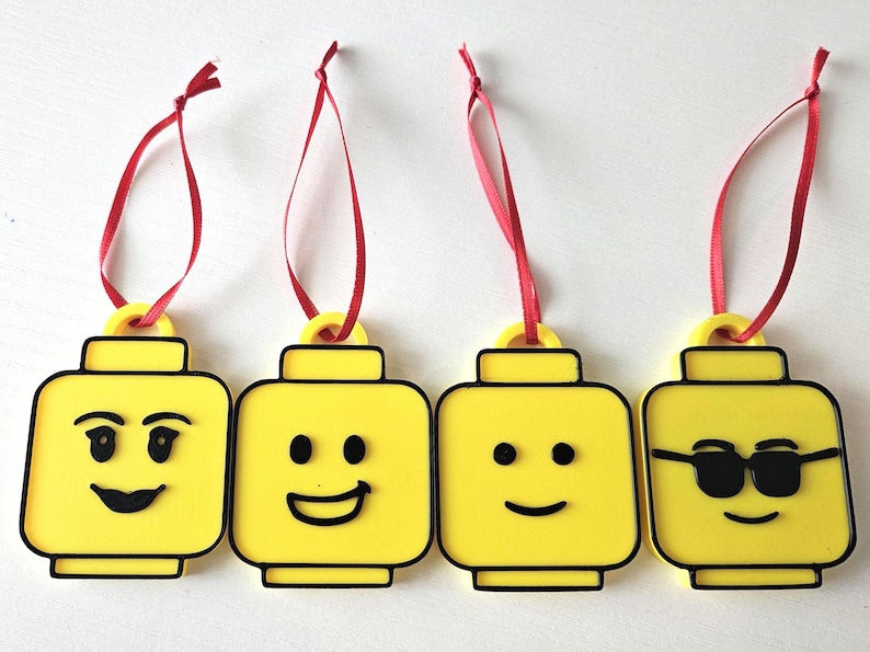 May include: Four yellow Lego minifigure ornaments with different facial expressions. Each ornament has a red ribbon for hanging.