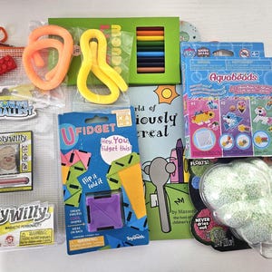 Pode incluir: Uma coleção de brinquedos e atividades infantis, incluindo um conjunto de lápis de cor, Aquabeads, um U Fidget e um jogo magnético Wooly Willy. Há também dois brinquedos coloridos e flexíveis e uma pequena bolsa laranja com zíper com um tijolo vermelho.