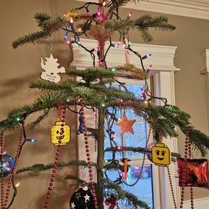 May include: A Christmas tree decorated with red and white beaded garlands, a yellow Lego minifigure ornament, a white ornament with the text "CRAIG INC 2018", a red and white star ornament, and a red and white ornament with the text "LOVE".