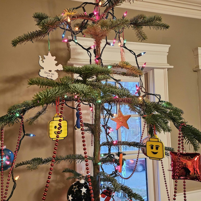 May include: A Christmas tree decorated with red and white beaded garlands, a yellow Lego minifigure ornament, a white ornament with the text "CRAIG INC 2018", a red and white star ornament, and a red and white ornament with the text "LOVE".