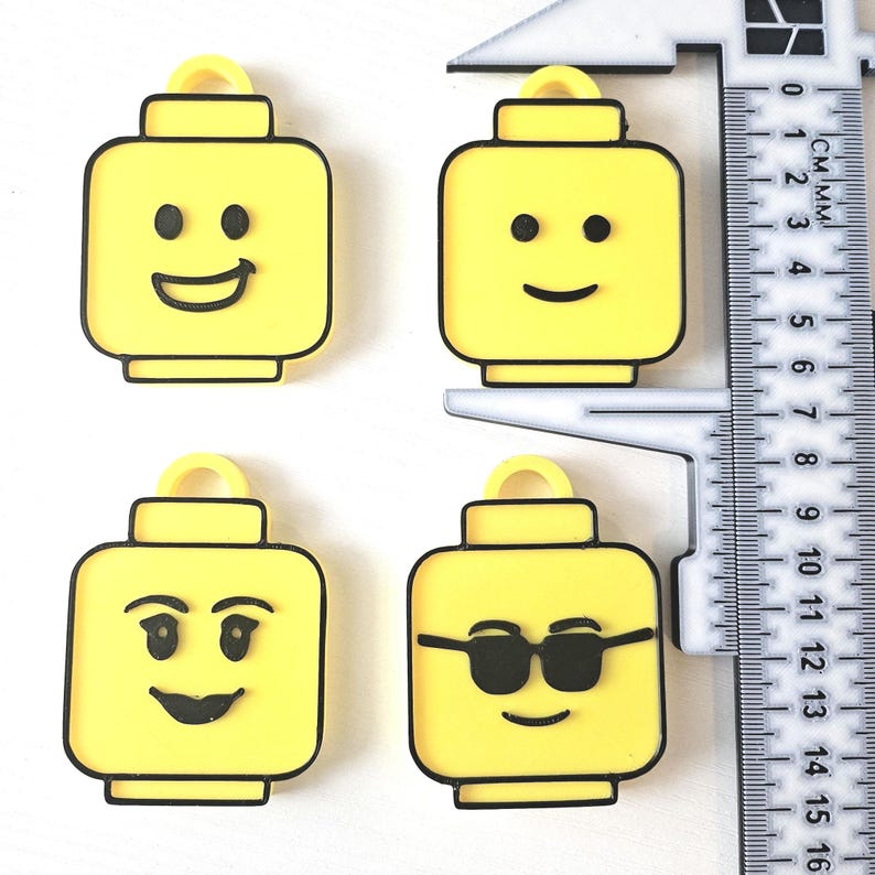 May include: Four yellow plastic Lego minifigure keychains with different facial expressions. The minifigures have black outlines and black facial features. The keychains are approximately 4 cm tall.