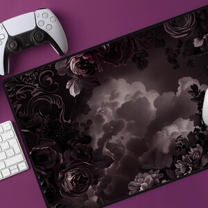 Op de afbeelding: Zwart-witte muismat met bloemenontwerp met een witte muis, toetsenbord en gamecontroller op een paars oppervlak. De muismat heeft een donker bloemenpatroon met rozen en wolken.