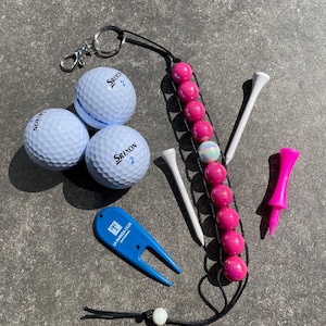 Puede incluir: Conjunto de accesorios de golf que incluye tres pelotas de golf Srixon blancas, un marcador de bola rosa con cuentas, una herramienta de reparación de divots azul y tees de golf blancos y rosas. Para el golf.