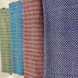 Può includere: Quattro asciugamani da cucina tessuti in diversi colori e motivi. Gli asciugamani sono verde, blu, rosso e blu con motivi geometrici bianchi.