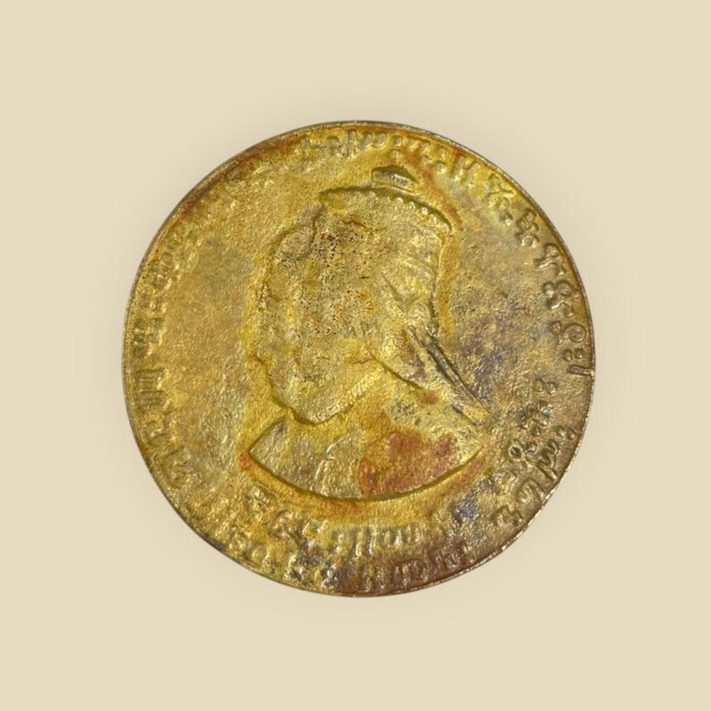 May include: A gold-colored coin with a profile of a woman wearing a crown. The coin has the inscription "VICTORIA REGINA 1837 - 1901" around the edge.
