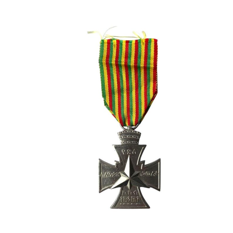 Puede incluir: Una medalla de plata con forma de cruz y una estrella en el centro. La medalla tiene los n&uacute;meros 1914-1918 y 1939-1945. La medalla est&aacute; unida a una cinta de rayas verdes, amarillas y rojas.
