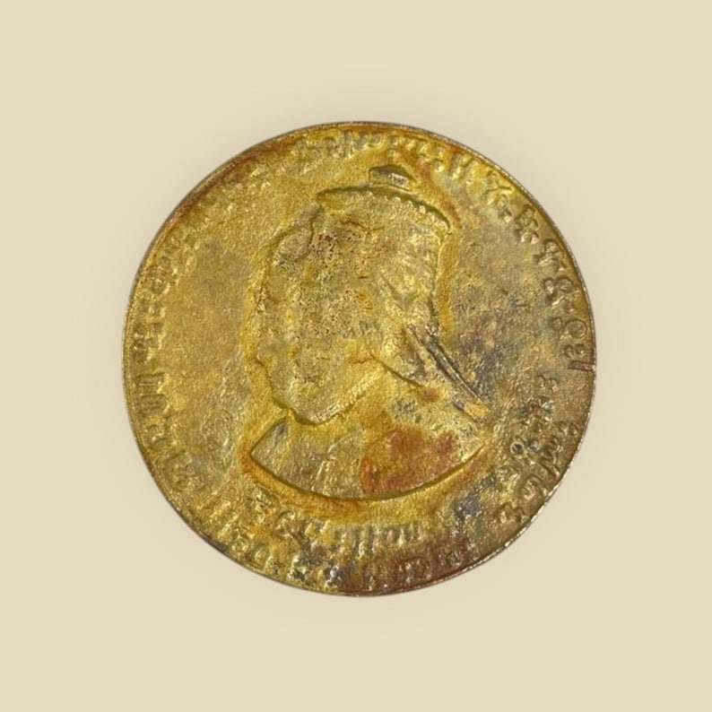 May include: A gold-colored coin with a profile of a woman wearing a crown on one side. The inscription on the coin reads "VICTORIA REGINA 1837 - 1861".