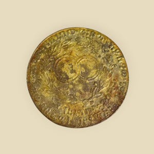 May include: A gold-colored metal coin with a wreath of leaves and two intertwined circles in the center. The inscription around the edge reads "UNITED STATES OF AMERICA 1792 ONE CENT".