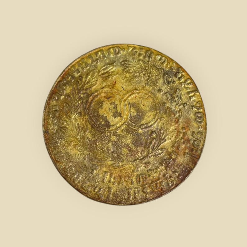 May include: A gold-colored metal coin with a wreath of leaves and two intertwined circles in the center. The inscription around the edge reads "UNITED STATES OF AMERICA 1792 ONE CENT".