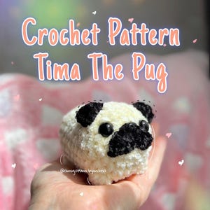 May include: A crocheted pug doll with black and white coloring is held in a hand. The text "Crochet Pattern Tima The Pug" is displayed above the doll. The doll has black eyes and a black nose. The doll is made of a soft, textured yarn.