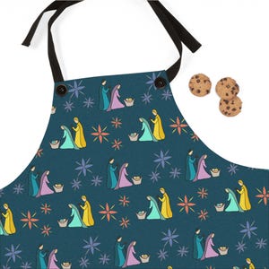 May include: A teal blue apron with a repeating pattern of the nativity scene. The pattern includes three figures, a star, and a basket. The figures are yellow, blue, pink, and green. The star is yellow with orange and red accents. The basket is brown.