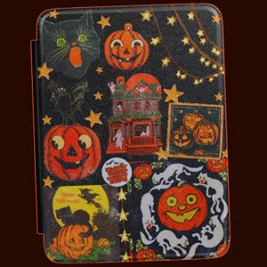 May include: A rectangular e-reader case with a black background featuring a Halloween pattern of orange jack-o'-lanterns, a haunted house, black cats, white ghosts, and yellow stars. A circular sticker reads Trick or Treat with a witch silhouette.
