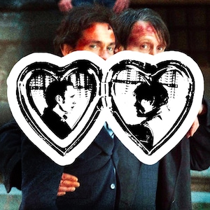 May include: A white heart-shaped locket graphic featuring a black and white illustration of two individuals in profile facing each other. The locket is open, displaying two separate heart-shaped frames, each containing a silhouette of a person.