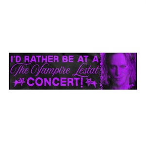 May include: A rectangular black banner with purple text that reads "I'D RATHER BE AT A The Vampire Lestat CONCERT!" with a purple image of a person on the right side. The text is in a stylized font with star accents.