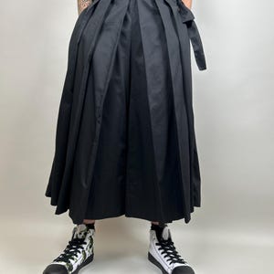 May include: Black pleated skirt with a wide waistband and a long, flowing silhouette. The skirt is made of a lightweight fabric and has a relaxed fit.