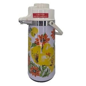 Puede incluir: Dispensador de bebidas vintage blanco y con estampado floral. El dispensador tiene una parte superior blanca con asa y una etiqueta roja que dice "CAUTION ADD ICE CAREFULLY". El cuerpo está decorado con grandes flores amarillas y naranjas.