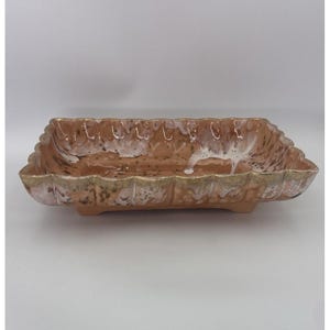 May include: A rectangular ceramic dish with a scalloped edge. The dish is primarily a warm brown color with white and gold accents. The interior has a speckled pattern, and the edges are textured.