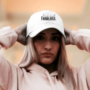 May include: White baseball cap with the text "Free and Fearless" embroidered in black.