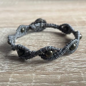 Può includere: Un braccialetto in macramé grigio con perline grigio scuro.
