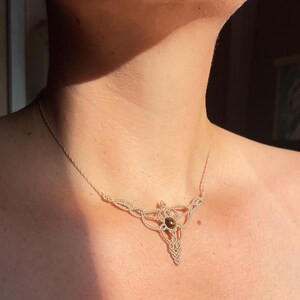 Op de afbeelding: Een beige macramé ketting met een bruine edelsteen hanger. De ketting is geknoopt in een geometrisch patroon.