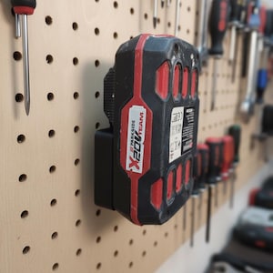 Könnte beinhalten: Ein schwarzer und roter Parkside X20V Team Akku an einer Lochwand befestigt. Der Akku hat rote Akzente und der Markenname ist sichtbar. Verschiedene Werkzeuge sind im Hintergrund.