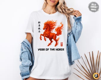 May include: White t-shirt featuring a vibrant orange illustration of a horse with flowing mane and tail. The design includes Chinese characters and the text "YEAR OF THE HORSE" in black. The shirt is a Bella Canvas brand.