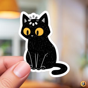 May include: A black cat sticker with large yellow eyes and a white border. The cat is sitting upright with its tail curled. The cat has a simple, cartoon-like design with a few white dots on its head.