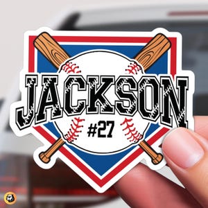 May include: A white baseball with red stitching and the name "JACKSON" #27 printed on it. Two crossed wooden baseball bats are behind the ball. The baseball is inside a blue and red baseball diamond.