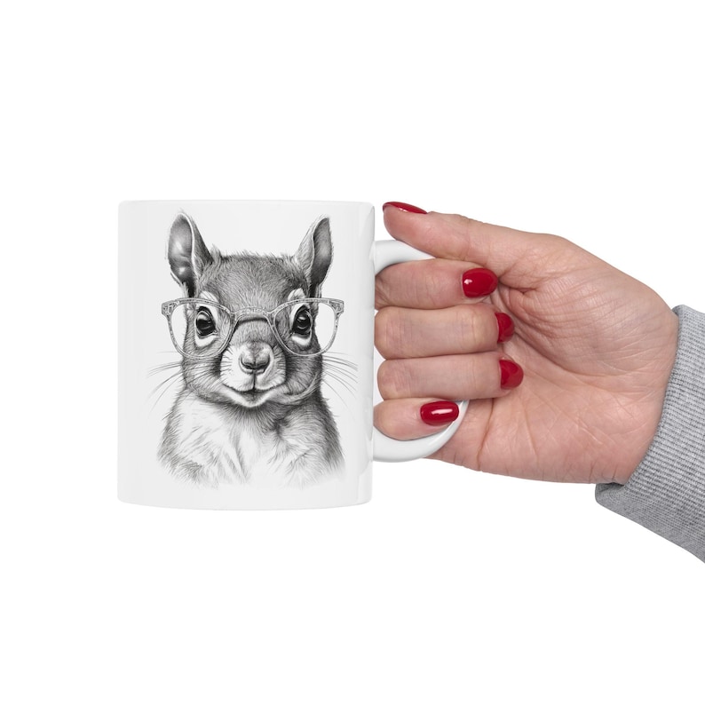 Pode incluir: Caneca de cer&acirc;mica branca com uma ilustra&ccedil;&atilde;o em preto e branco de um esquilo usando &oacute;culos. O esquilo est&aacute; olhando diretamente para o espectador.