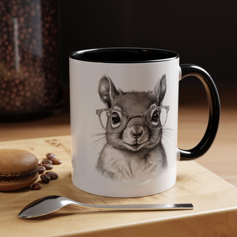 Pode incluir: Uma caneca de cer&acirc;mica branca com uma borda e uma al&ccedil;a pretas. A caneca apresenta uma ilustra&ccedil;&atilde;o em preto e branco de um esquilo usando &oacute;culos.