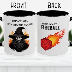 Może przedstawiać: Biały kubek ceramiczny z czarnym rantem i uchwytem. Przód kubka przedstawia kreskówkowego czarodzieja z brodą i spiczastym kapeluszem. Tekst na kubku brzmi "Nie pytałem, jak duży jest pokój". Tył kubka przedstawia czerwoną 20-ścienną kostkę do gry z płomieniami wychodzącymi z niej. Tekst na odwrocie kubka brzmi "Powiedziałem, że rzucam kulą ognia".