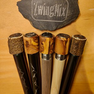 May include: Five wooden pen or pencil holders with different wood grain patterns and metal accents. The holders are arranged in a row on a wooden surface. The text "ZwingNix" is engraved on a black slate tile above the holders.