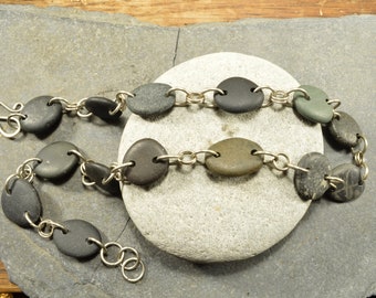 May include: A silver chain necklace with smooth, oval-shaped stones in shades of gray and green. The stones are connected by silver links.