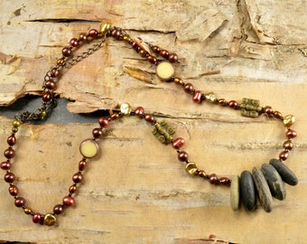 May include: A brown and gold necklace with a variety of beads, including round, oval, and rectangular shapes. The necklace also features a cluster of smooth, grey stones.