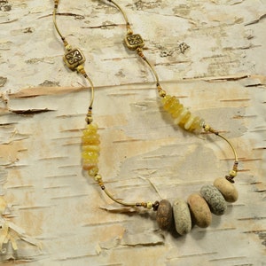 May include: A gold necklace with a variety of beads, including small round beads, larger flat beads, and a cluster of small, round, yellow beads. The necklace is on a birch bark background.