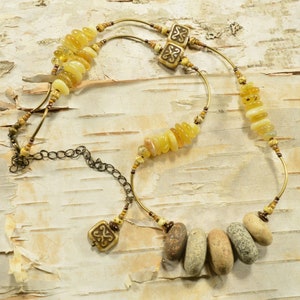 May include: A multi-strand necklace with yellow and brown beads, including a cluster of smooth, gray stones. The necklace features two brass charms with a Celtic knot design.