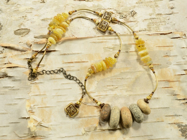 May include: A multi-strand necklace with yellow and brown beads, including a cluster of smooth, gray stones. The necklace features two brass charms with a Celtic knot design.