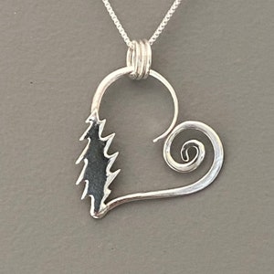May include: A silver pendant necklace featuring a heart-shaped design with a stylized tree on one side and a spiral on the other. The pendant hangs from a delicate chain, showcasing a nature-inspired theme.