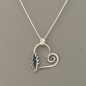 May include: A silver pendant necklace featuring a heart-shaped design. The pendant has a stylized tree on one side and a spiral on the other. The necklace chain is a delicate silver chain.