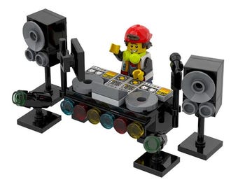 Può includere: Un set console DJ in mattoncini di plastica composto da un mixer centrale con due piatti, una minifigure con cappellino rosso, due torri di altoparlanti nere, un microfono su asta e una fila di luci circolari traslucide multicolori.