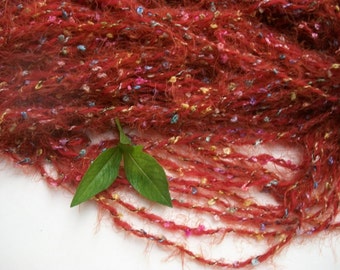 May include: A close-up of a red yarn with multi-colored flecks. The yarn is soft and fluffy, and it is perfect for knitting or crocheting.