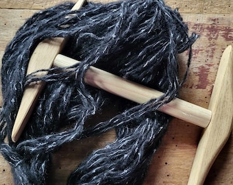 May include: A close-up of a wooden spinning wheel with a black and white yarn skein. The spinning wheel has a wooden handle and a spindle.