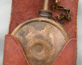 May include: A brown leather pouch with a brass oiler inside. The pouch has a snap closure and a metal ring. The oiler has a chain attached to it.