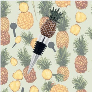 Może przedstawiać: Srebrny korek do butelki w kształcie ananasa z czarną gumową zatyczką. Korek do butelki znajduje się na tle powtarzającego się wzoru ananasów.