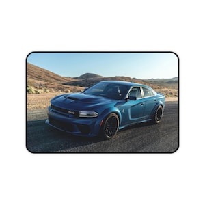 May include: A blue sports car with black wheels is parked on a paved road. The car has a sleek design and is set against a backdrop of desert hills and a clear blue sky. The car has a hood scoop.
