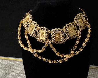 May include: A gold-colored necklace with rectangular pendants and dangling chains. Each pendant features a floral design. The necklace is displayed on a black mannequin, showcasing its intricate details and craftsmanship.