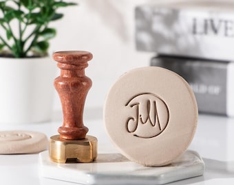May include: A wooden stamp with a brass base and a round, beige wax seal with the word "Jill" inscribed in cursive.